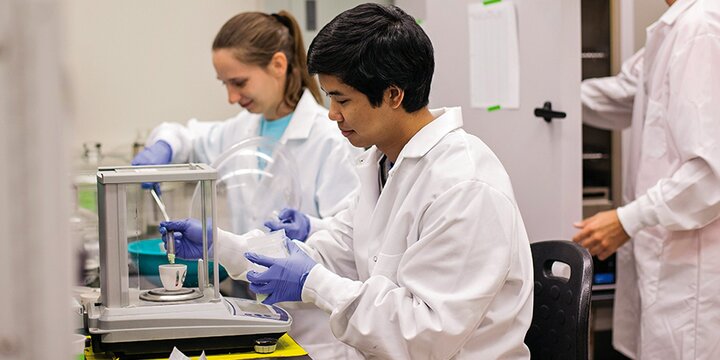 Students in lab coats working in lab.