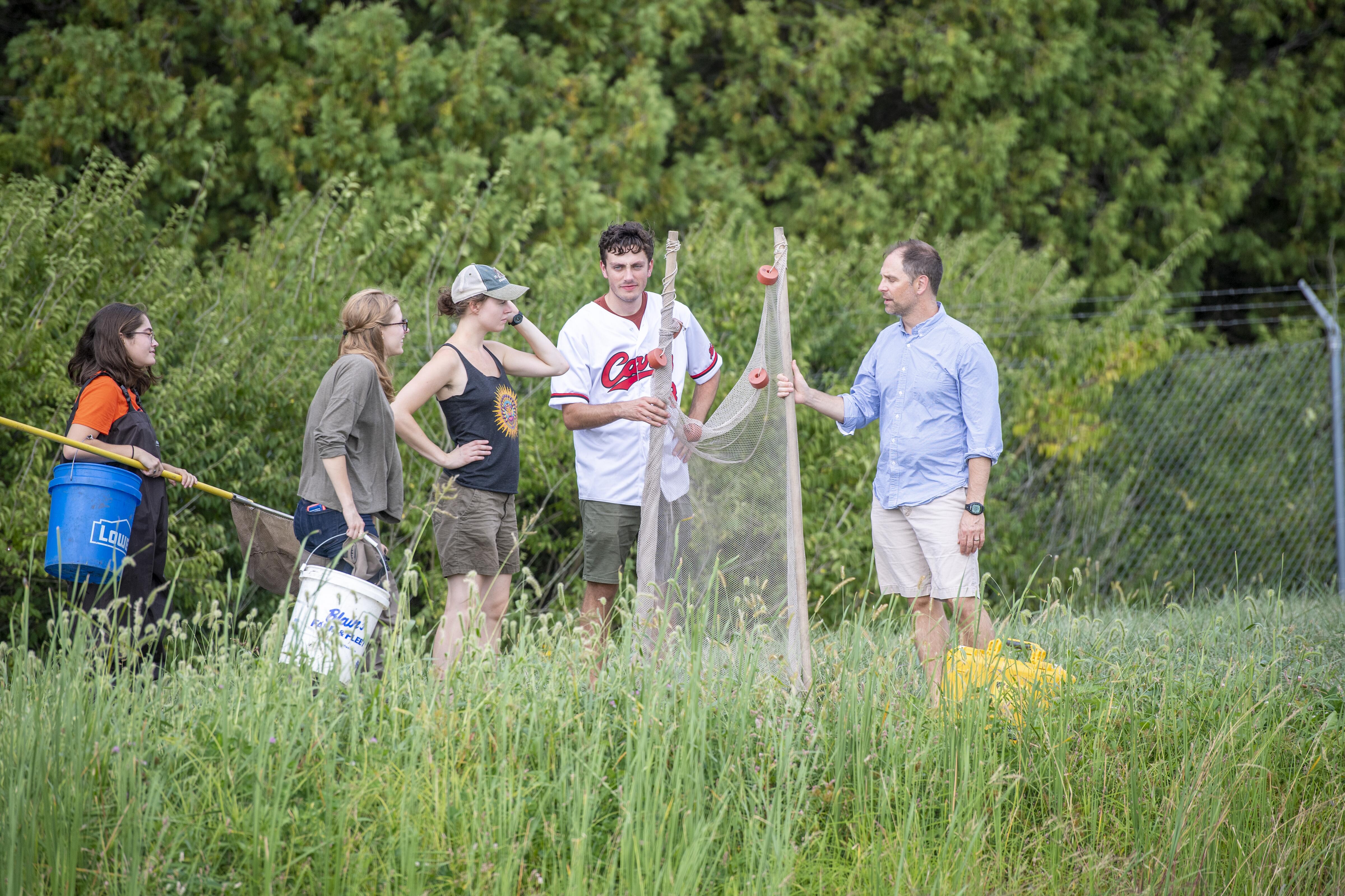 Students in a river bank with fish nets.