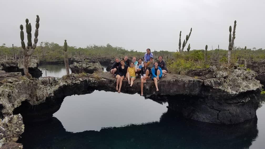 Study abroad students sitting on a rock above a body of water